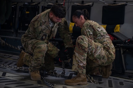 Two Airmen tie down cargo on a plane.