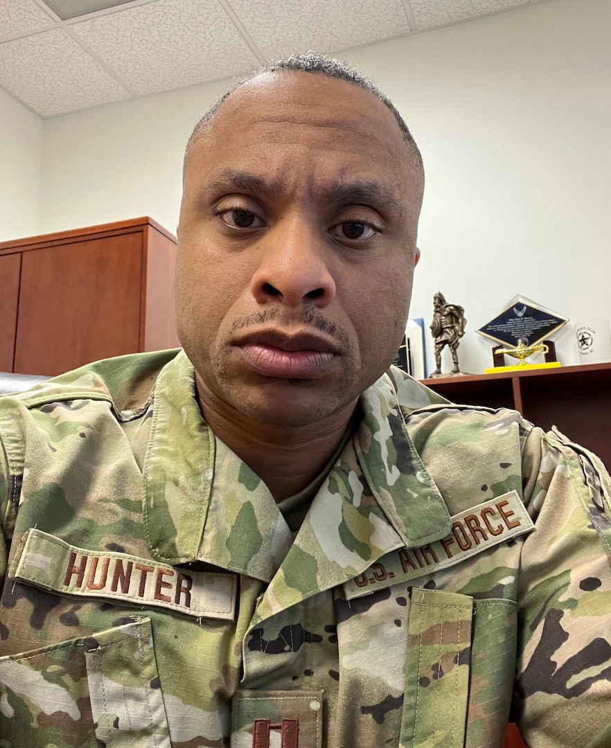 Medium close portrait of African American man in U.S. Air Force dress blue shirt and tie. He's wearing a serious look and looking at the camera.