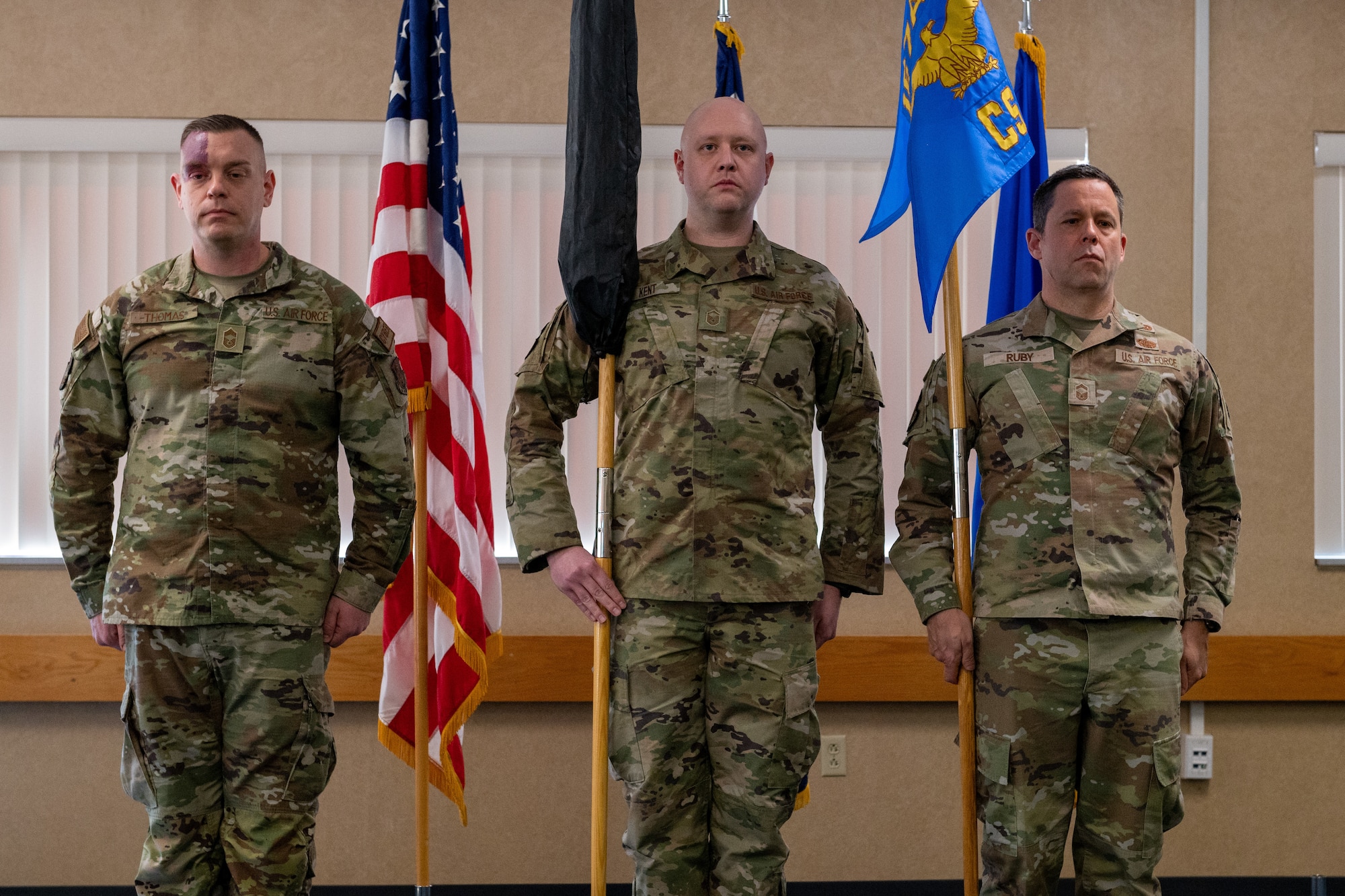 three men stand at attention, two of them are holding guidons