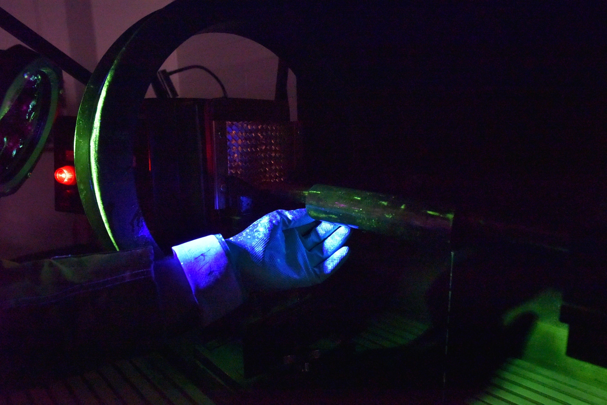 A gloved hand turns a cylinder lit with blacklight.