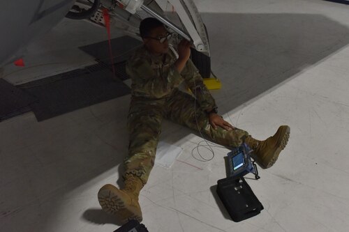 An Airmen sits under an aircraft with a diagnostic instrument.