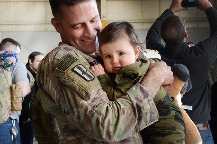 Sgt. 1st Class Jeff Stainsby, A Battery, 182nd Field Artillery, Michigan National Guard, holds his daughter, Clair, for the first time at the unit’s welcome home ceremony in Detroit, Mich, Feb. 8, 2024.