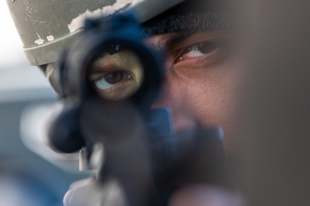 An airman looks through the scope of a gun.