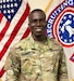 man wearing u.s. army uniform standing in front of two flags.