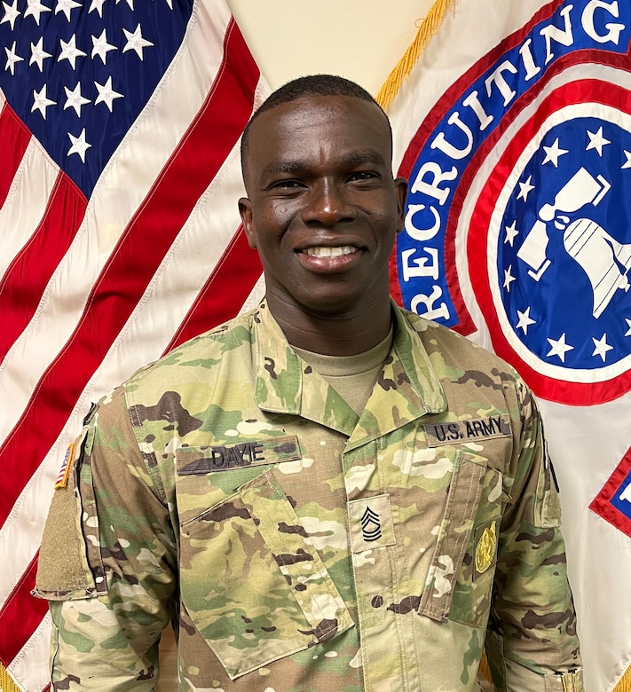 man wearing u.s. army uniform standing in front of two flags.