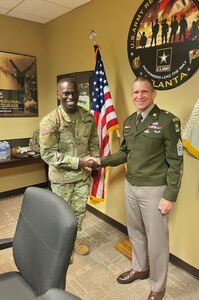 two men wearing u.s. army uniforms shake hands in a recruiting office.