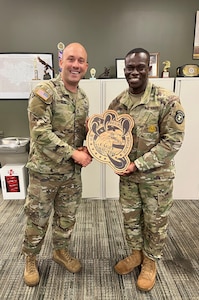 two men wearing u.s. army uniforms shake hands in a recruiting office.