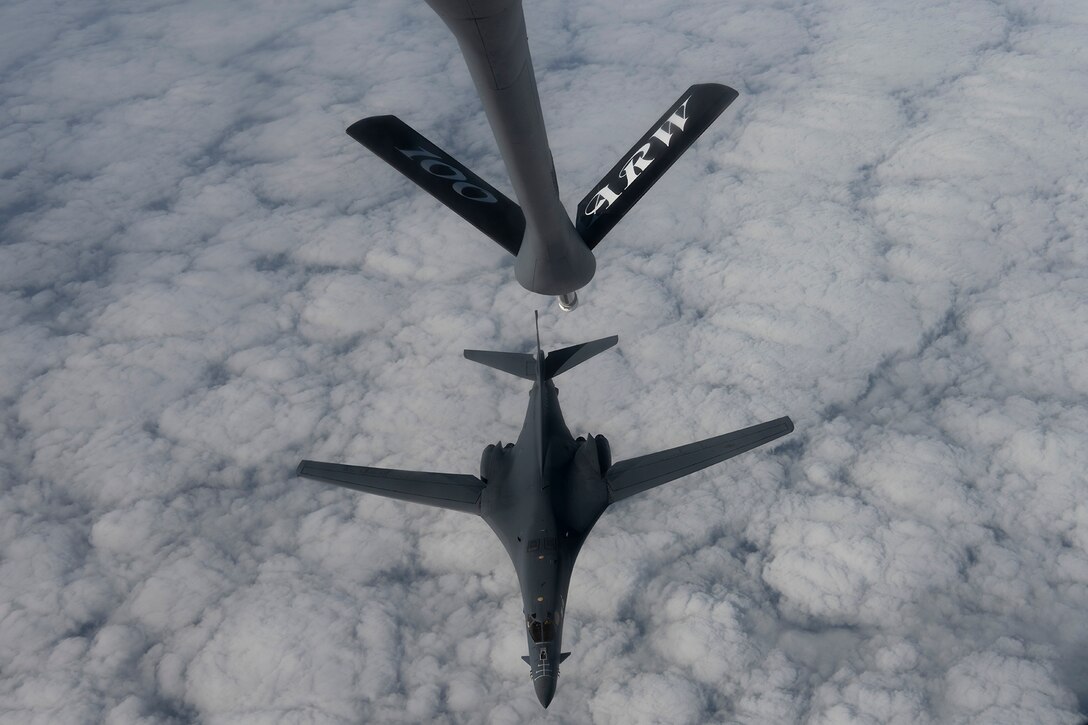 A military aircraft detaches from another after receiving fuel in flight. The aircraft is photographed from above and clouds are visible.