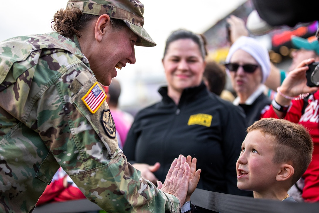 A uniformed service member high-fives a child.