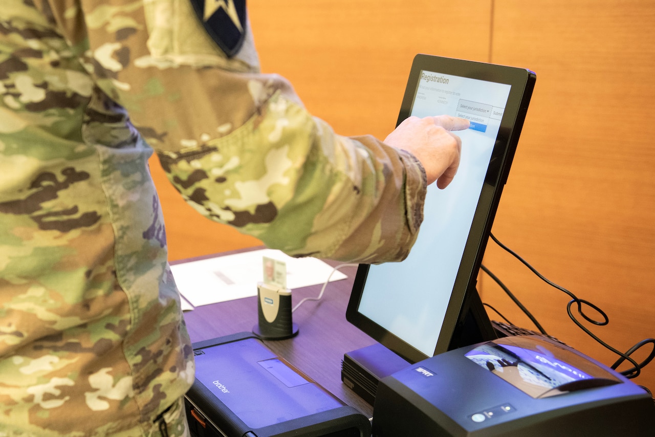 A service member in uniform touches a screen that says “registration.”