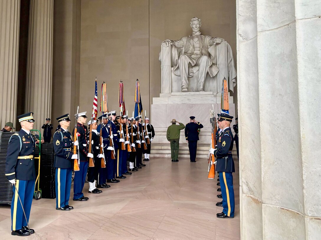 Joint troops stand in two lines flanking Abraham Lincoln's statue at his memorial, as two officials salute at its base.