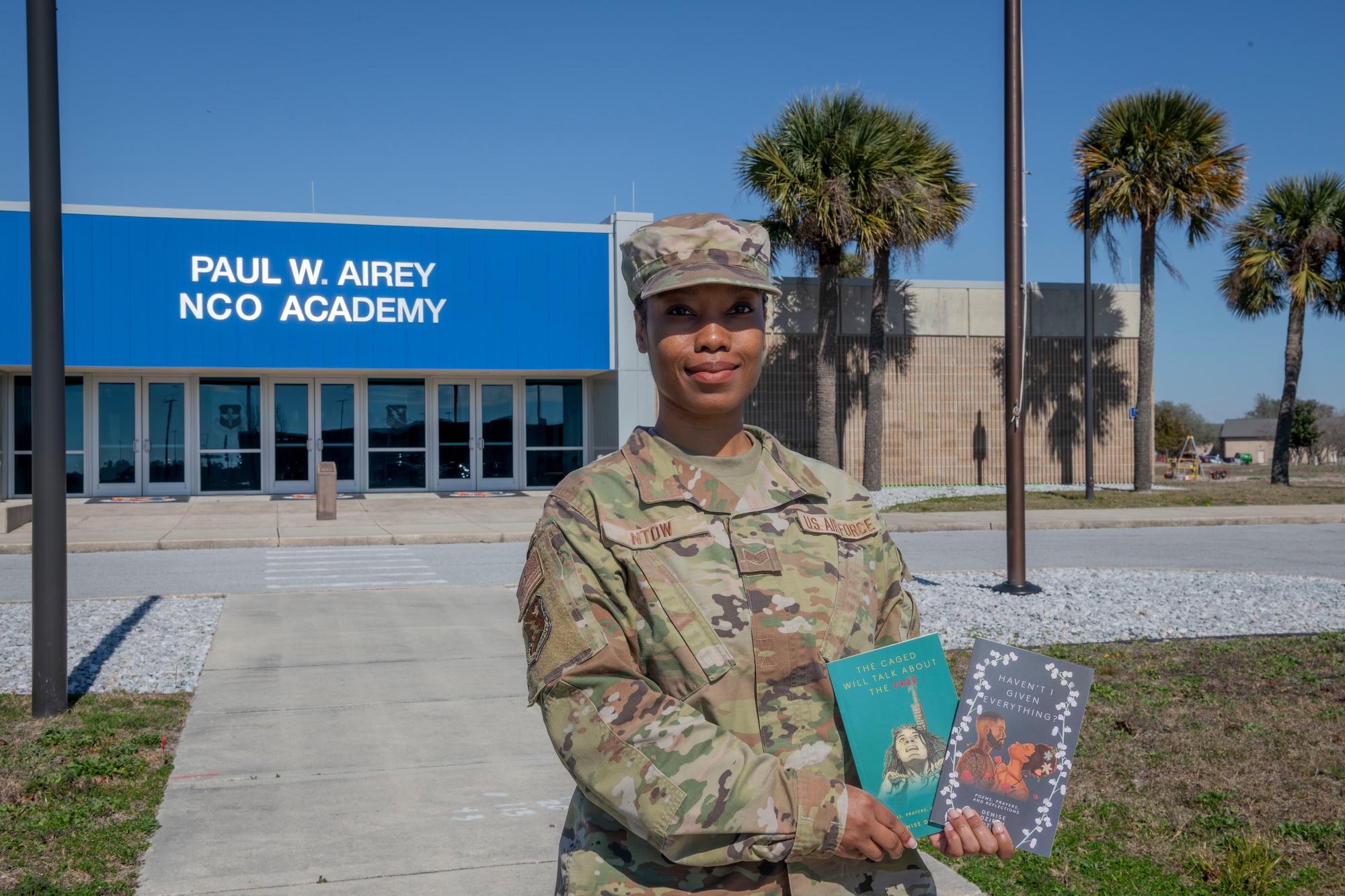 An Airman poses for a photo holding two books.
