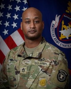 man wearing u.s. army uniform poses in front of two flags.