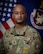 man wearing u.s. army uniform poses in front of two flags.