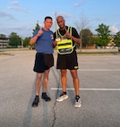 two men wearing u.s. army black PT uniform pose together.