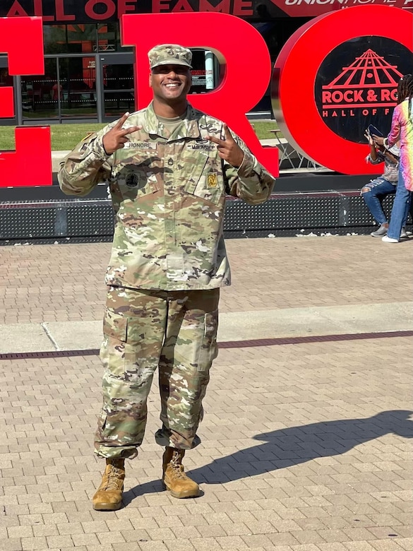 man wearing u.s. army uniform standing in an open area in a park.