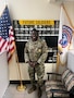 man wearing u.s. army uniform standing in front of a wall with two flags.