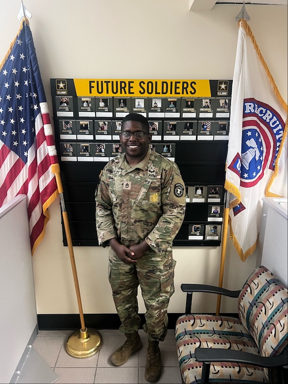 man wearing u.s. army uniform standing in front of a wall with two flags.