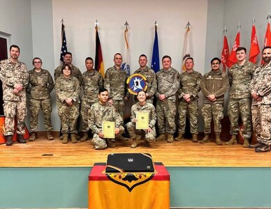 Two Airmen pose for a photo with their German Armed Forces Proficiency Badge certificates.