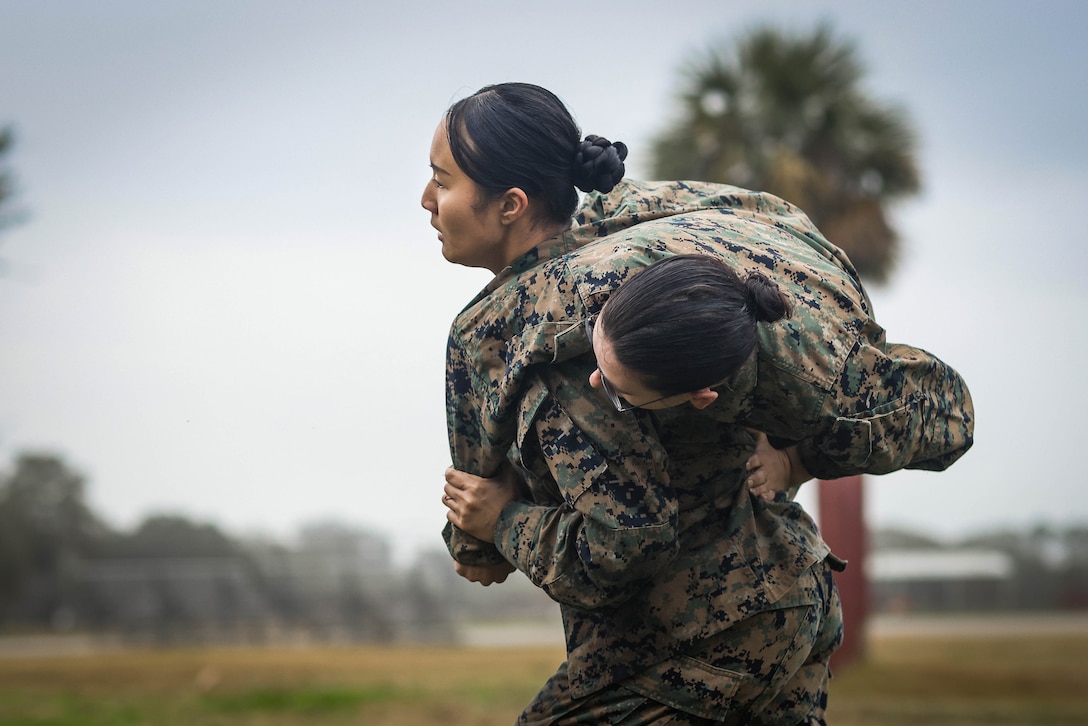 A uniformed Marine carries another over their shoulder.