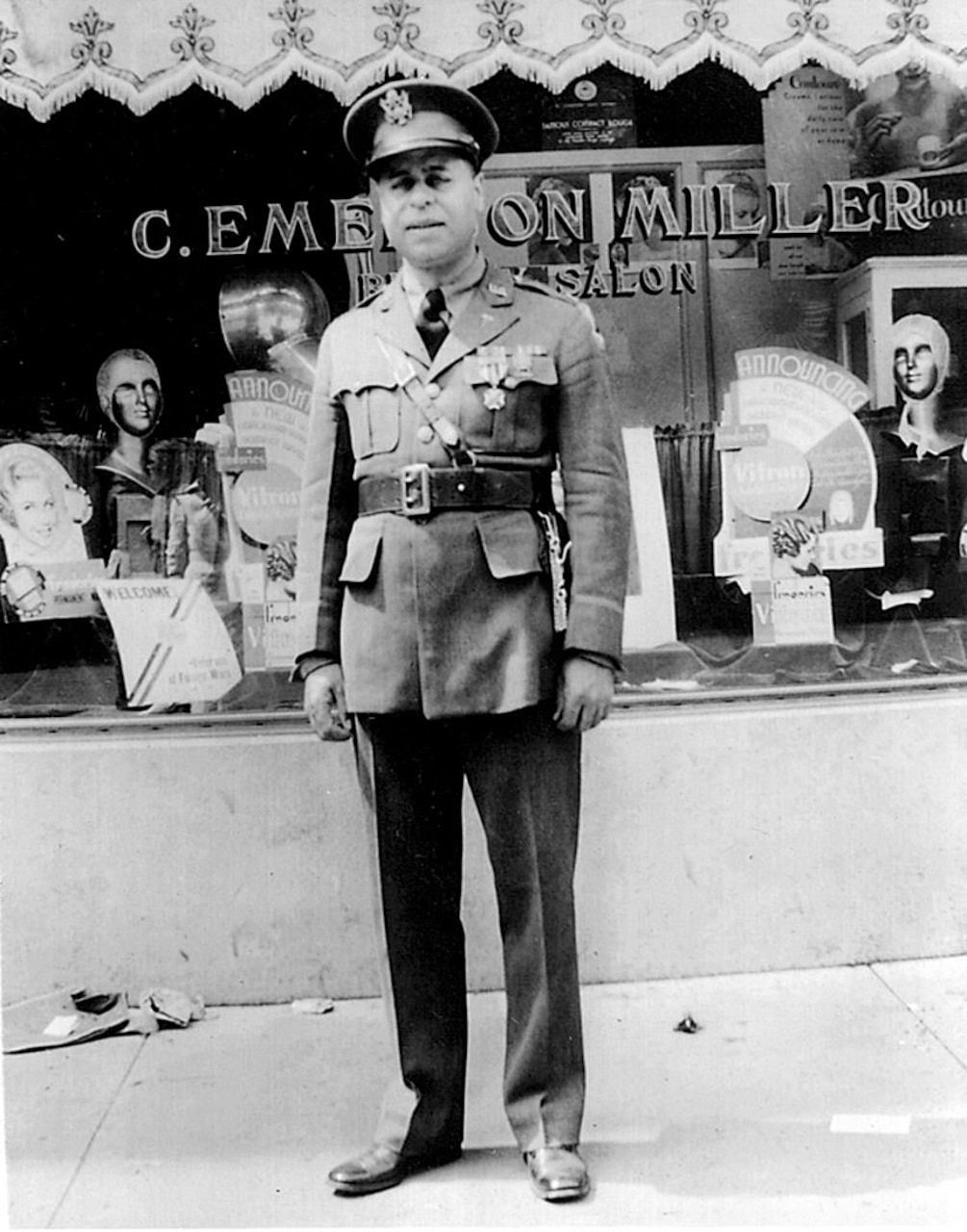 A person in a military uniform stands in front of a storefront.