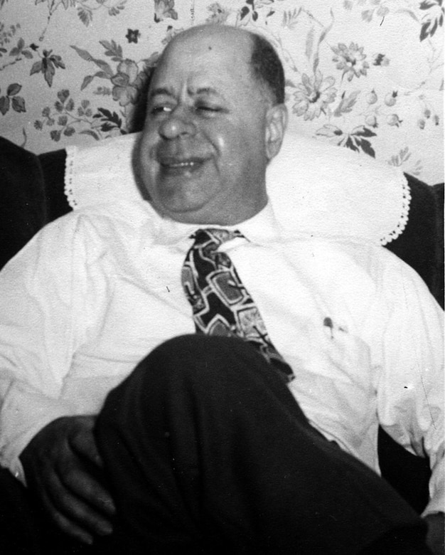 A seated person in a tie smiles.