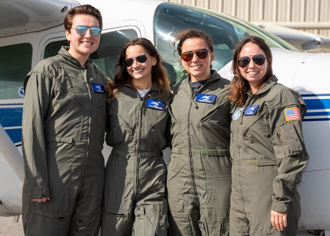 Four female pilots wearing sunglasses stand in front of a small plane.