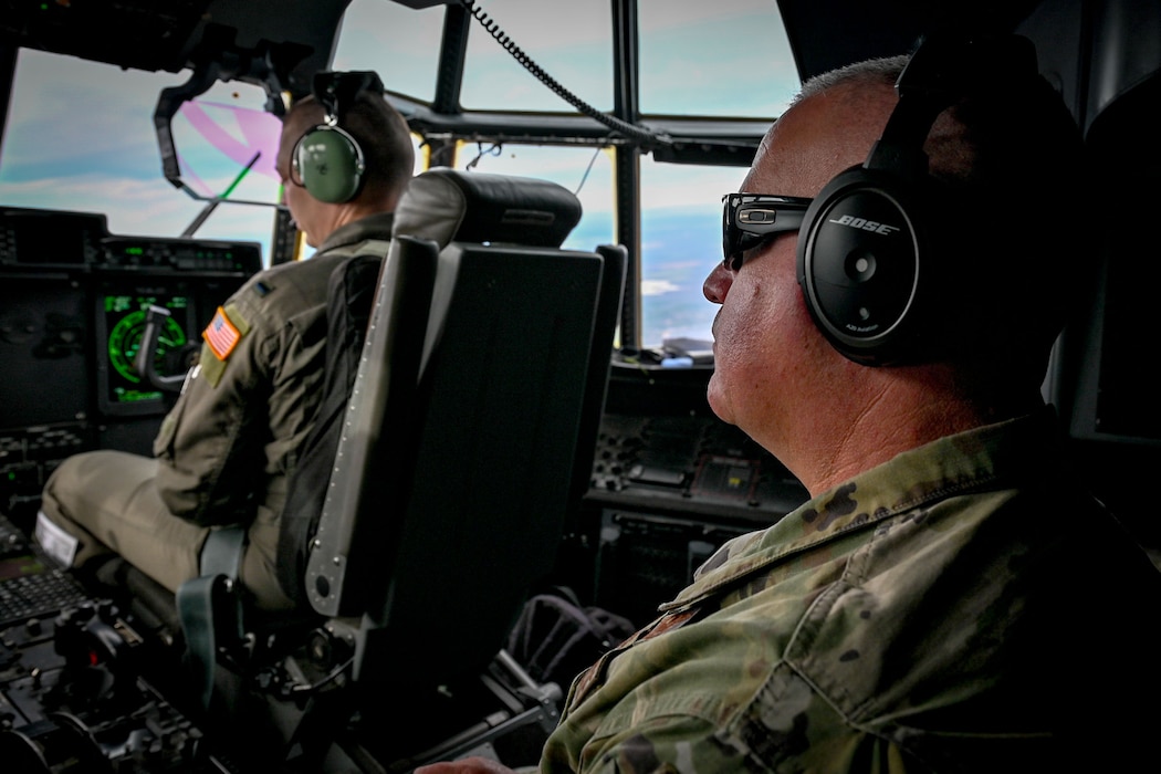Two Airmen sit in the cockpit of a flying C-130J Super Hercules aircraft