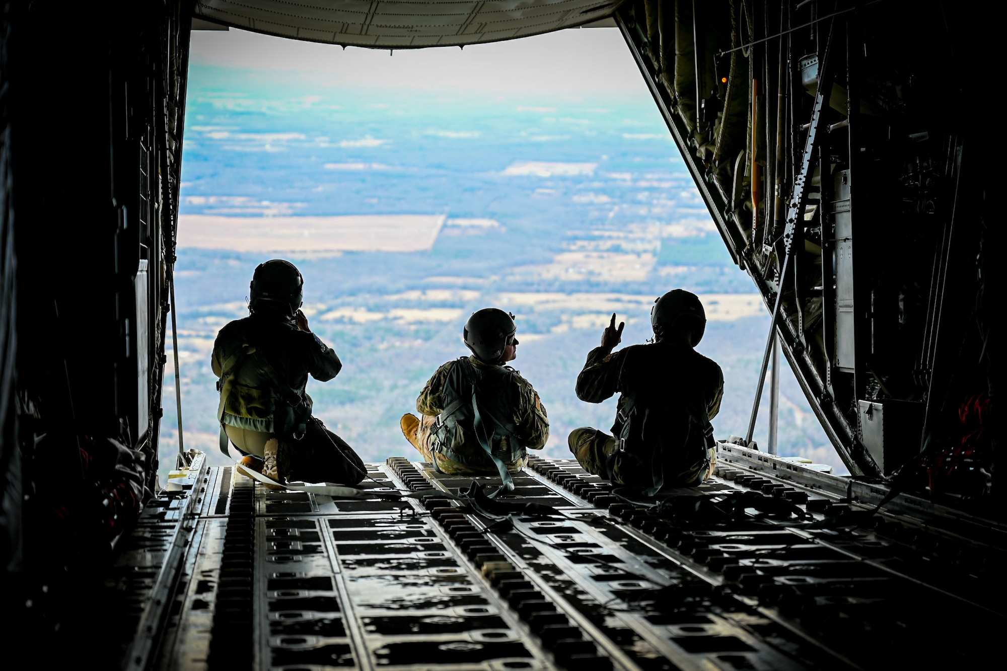 Three Airmen sit in the back of a flying a C-130J Super Hercules aircraft