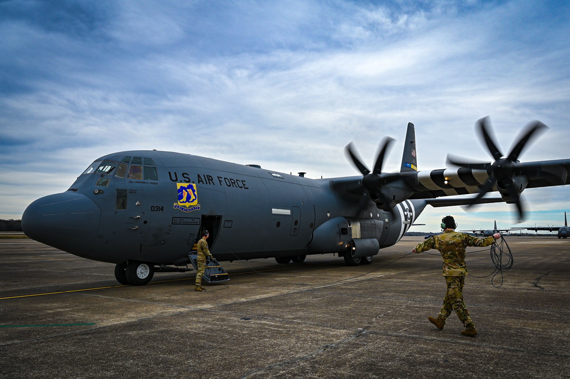 Two Airmen wrapping a cord in front of a C-130J Super Hercules aircraft