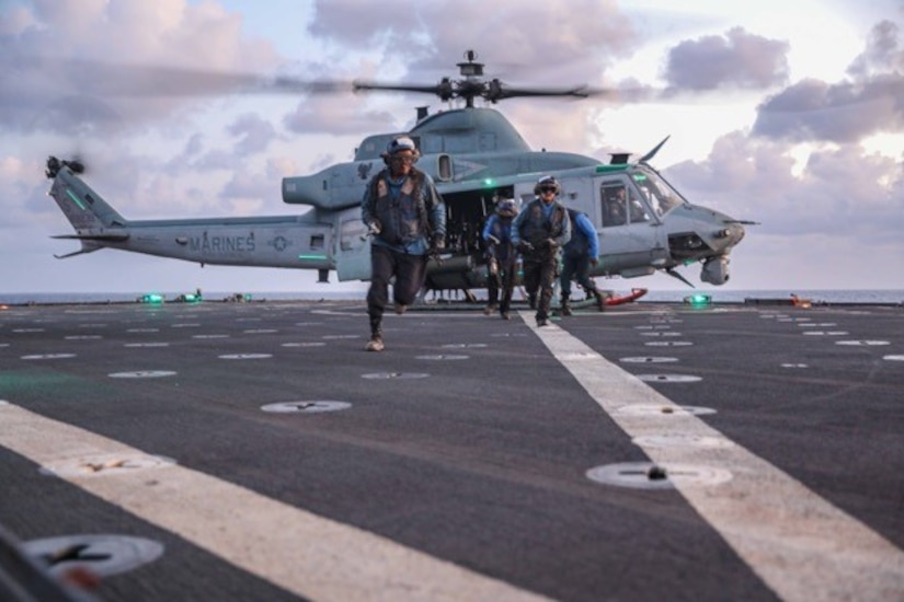 Sailors run from a helicopter aboard a ship at sea.