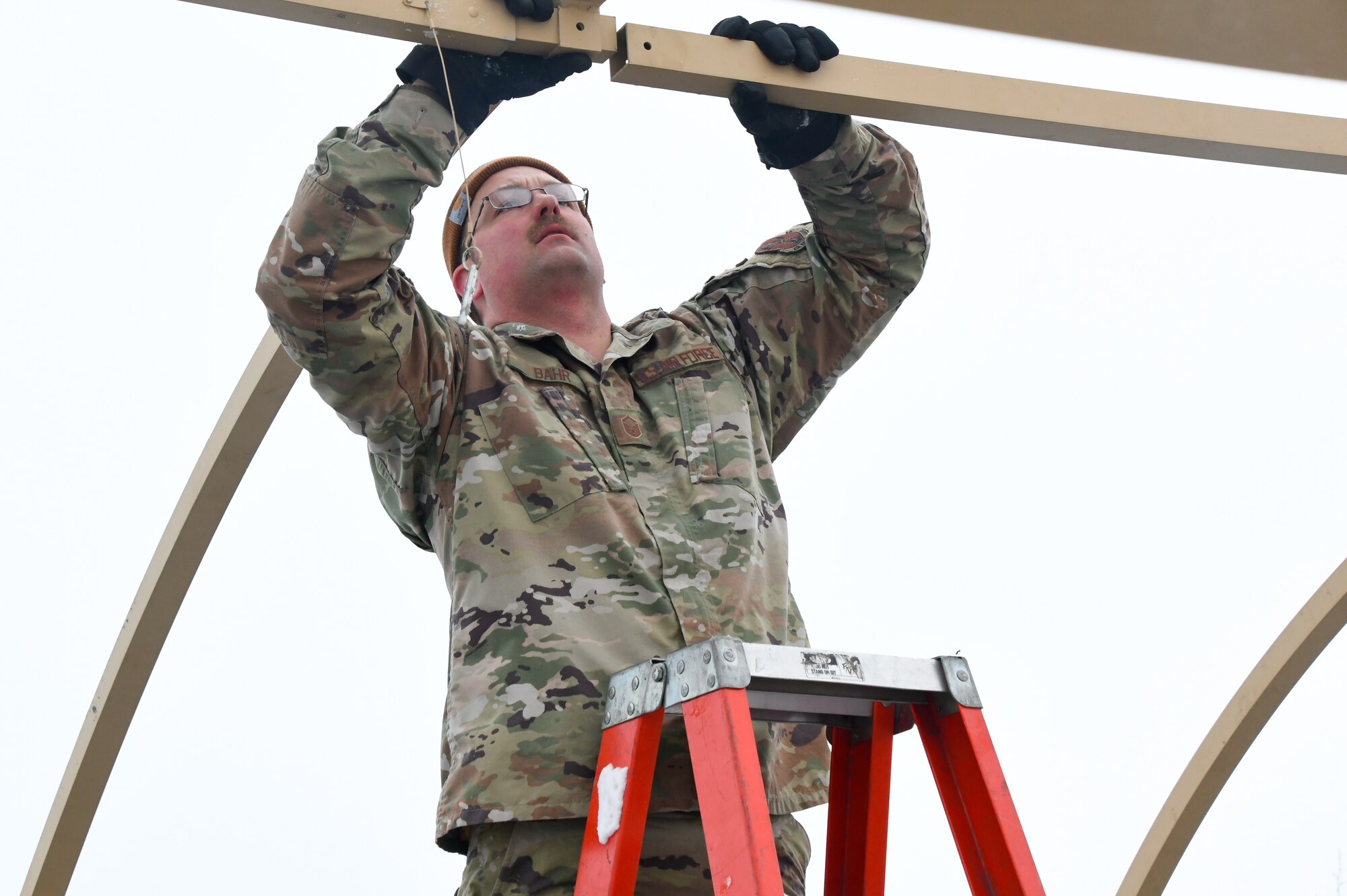 U.S. Air Force Master Sgt. Michael Bahr, Civil Engineer Operations Manager, 168th Civil Engineer Squadron, attaches a beam while configuring a tent set up with a team of Airmen during agile combat employment training at Fort Greely Donnelly Training area.