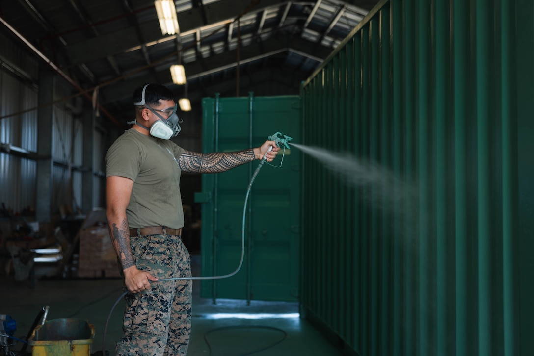 U.S. Marine Corps Sgt. Rasheed Awyan spray paints a quadcon on Marine Corps Base Hawaii, Feb. 12, 2024. 3d Littoral Logistics Battalion is experimenting with mobile structural sleeping quarters in preparation for future training opportunities. The sleeping quarters can hold up to 6 Marines and contain racks to hold gear, electrical appliances such as lights and air conditioning, and other storage space. Awyan is an engineer equipment operator with 3d LLB, 3d Marine Littoral Regiment, 3d Marine Division and is a native of Kailua-Kona, Hawaii. (U.S. Marine Corps photo by Cpl. Eric Huynh)