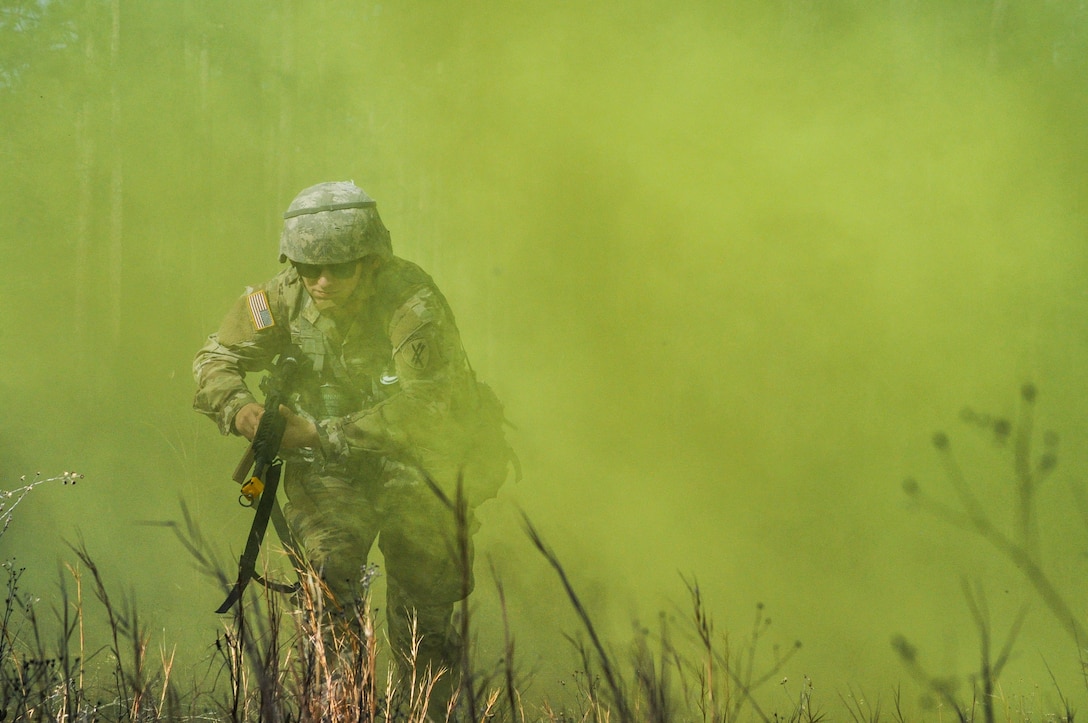A soldier carrying a weapon runs through a field covered in yellow smoke.