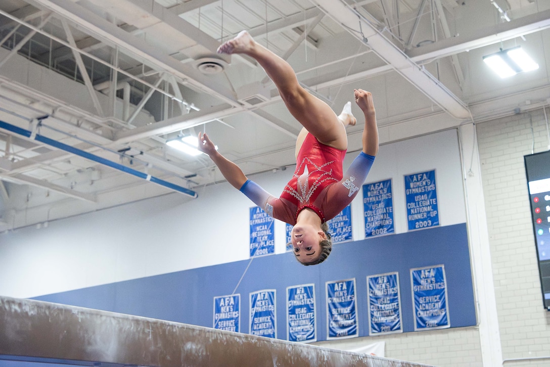 A gymnast flips on the balance beam.