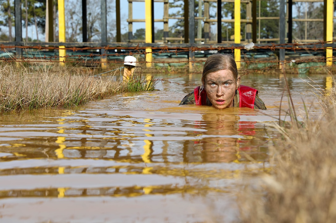 A service member swims through muddy water.