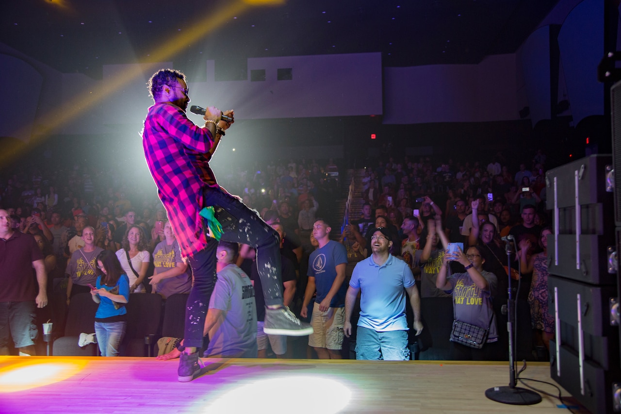 A man in casual clothes sings into a microphone.