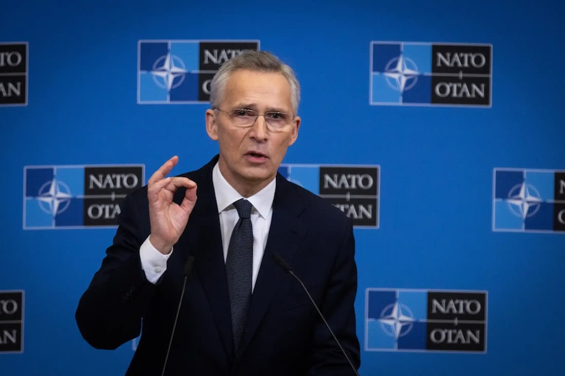 A man in business attire, standing at a microphone, gestures as he speaks. The backdrop indicates that he is at NATO.