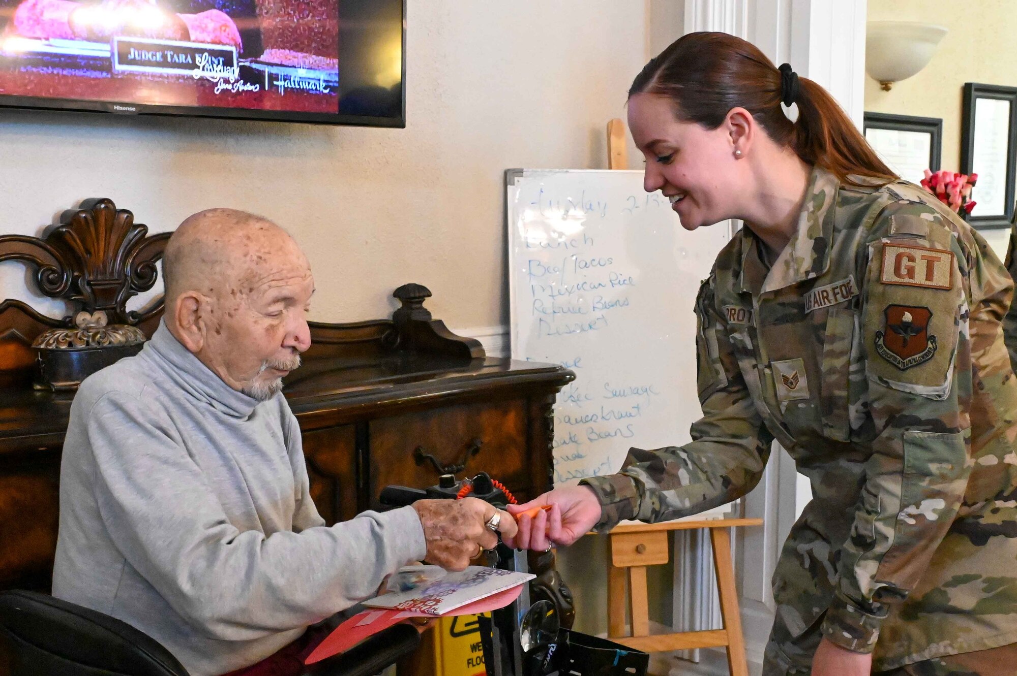 Dallas Gibbs, a retired Airman, takes a bag of candy from Staff Sgt. Pamela Proteau, 97thLogistics Readiness Squadron noncommissioned officer in charge of ground transportation, at Magnolia Creek in Altus, Oklahoma, Feb. 14, 2024. Gibbs served as an aircraft mechanic in the Air Force for 22 years. (U.S. Air Force photo by Airman 1st Class Kari Degraffenreed)