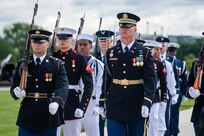 Members from various branches of the military are marching toward the camera. Most have a rifle on their right shoulder.