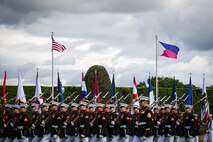 Marines in dress uniforms are marching with rifles on their shoulders as the flags of the US and the Philippines are flying behind them.