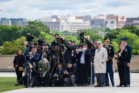 A large gaggle of photojournalists wearing various attire is pictured as they way to document a ceremony.