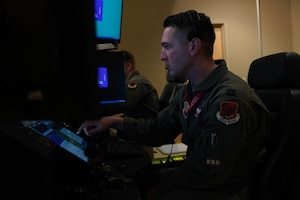 A man in a flight suit stares intensely at an aircraft simulator screen.