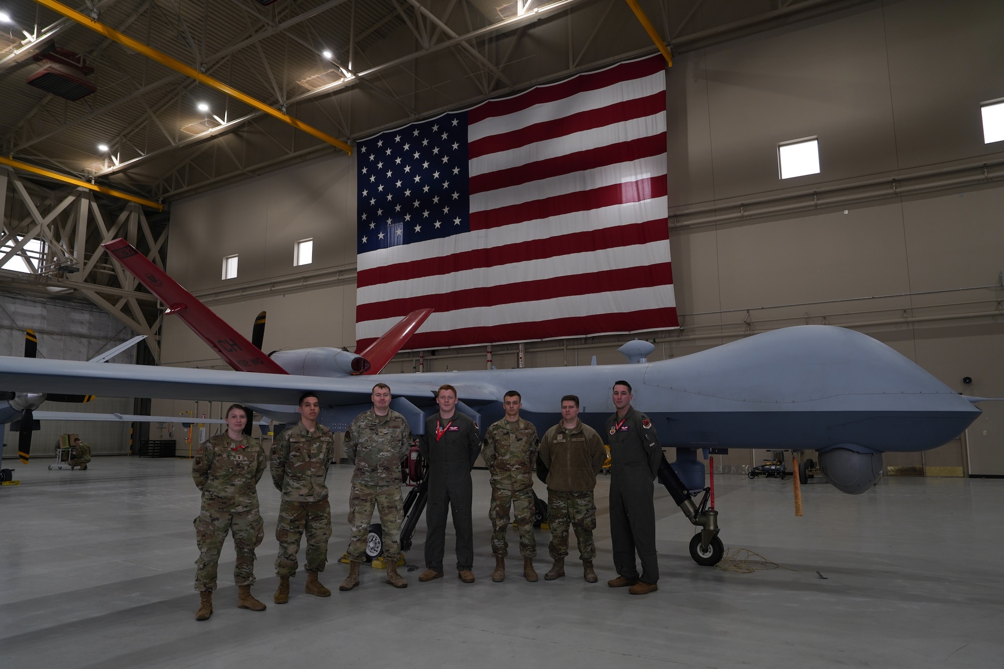 A group of people in military uniforms stand posed in front of a remotely piloted aircraft.