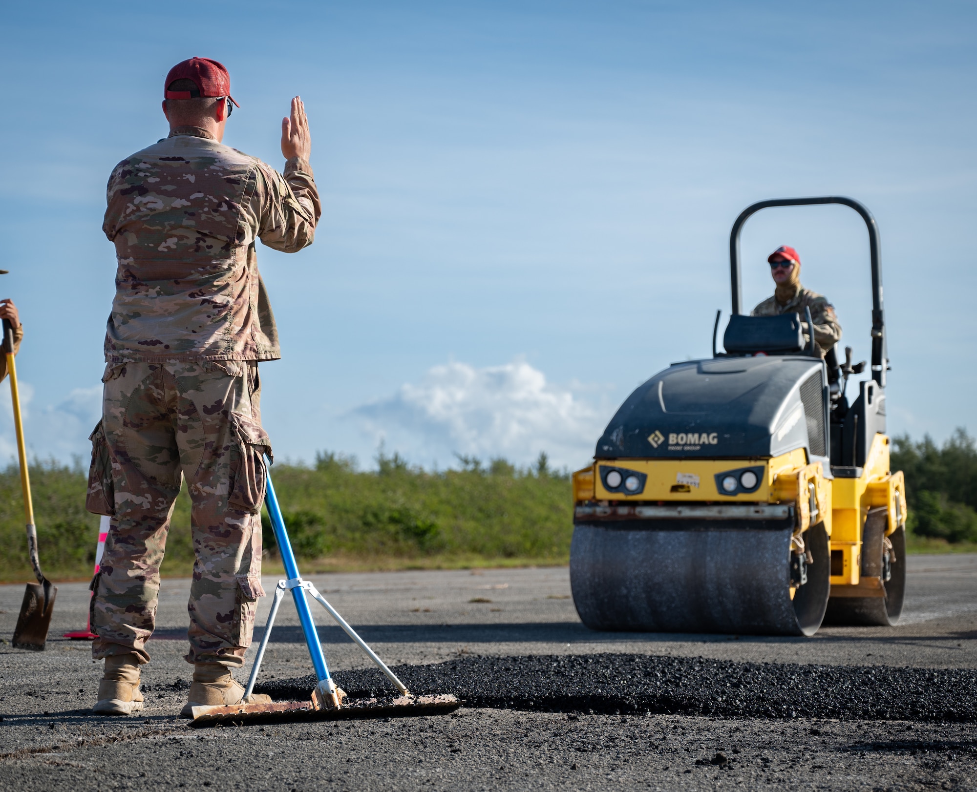 Tech. Sgt. Robert Belcher, 554th Rapid Engineering Deployable Heavy Operations Repair Squadron Engineer structural supervisor, guides Tech. Sgt. Austin Alfreno, 554th REDHORSE electrical contingency instructor, before he compacts fresh asphalt on Naval Base Guam, Feb. 8, 2024. The 554th REDHORSE have been working on NBG for a week to rehabilitate the flight line there. The flight line required re-pavement of many areas all of which only took the REDHORSE two days to assess and correct. (U.S. Air Force photo by Staff Sgt. Pedro Tenorio)