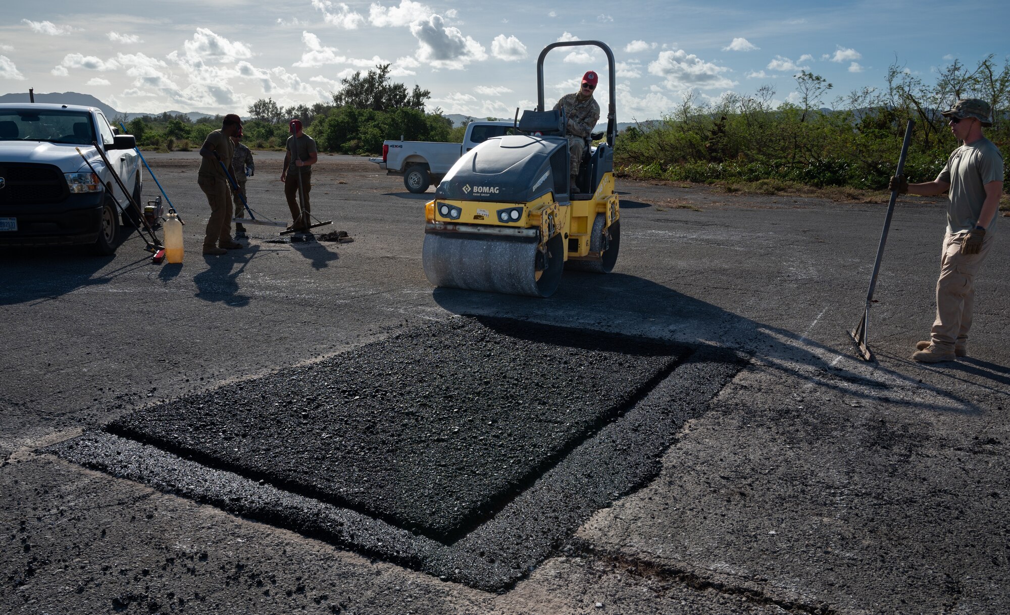554th Rapid Engineering Deployable Heavy Operations Repair Squadron Engineer heavy equipment and pavement Airmen repair Naval Base Guam's flight line, Feb. 8, 2024. On a previous day, REDHORSE Airmen scouted areas on the flight line deemed to damaged, these areas were then cut up and filled with new asphalt. The Airmen around with rakes were responsible to spread the asphalt neatly or remove excess asphalt and once complete the asphalt is compacted and smoothed over by the compaction roller. (U.S. Air Force photo by Staff Sgt. Pedro Tenorio)