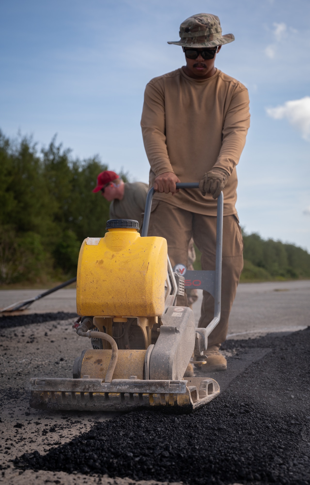 Airman 1st Class Jhunel Binoya, 554th Rapid Engineering Deployable Heavy Operations Repair Squadron Engineer heavy equipment and pavement specialist, uses a stamper machine to smooth out fresh asphalt on Naval Base Guam's flight line, Feb. 8, 2024. The 554th REDHORSE have been hard at work for a week clearing and rehabilitating the flight line on NBG. Their efforts are part of a larger plan to expand aircraft capabilities on Guam as simultaneous flight line rehabilitation efforts occur on Pacific Regional Training Center - Andersen, Guam. (U.S. Air Force photo by Staff Sgt. Pedro Tenorio)