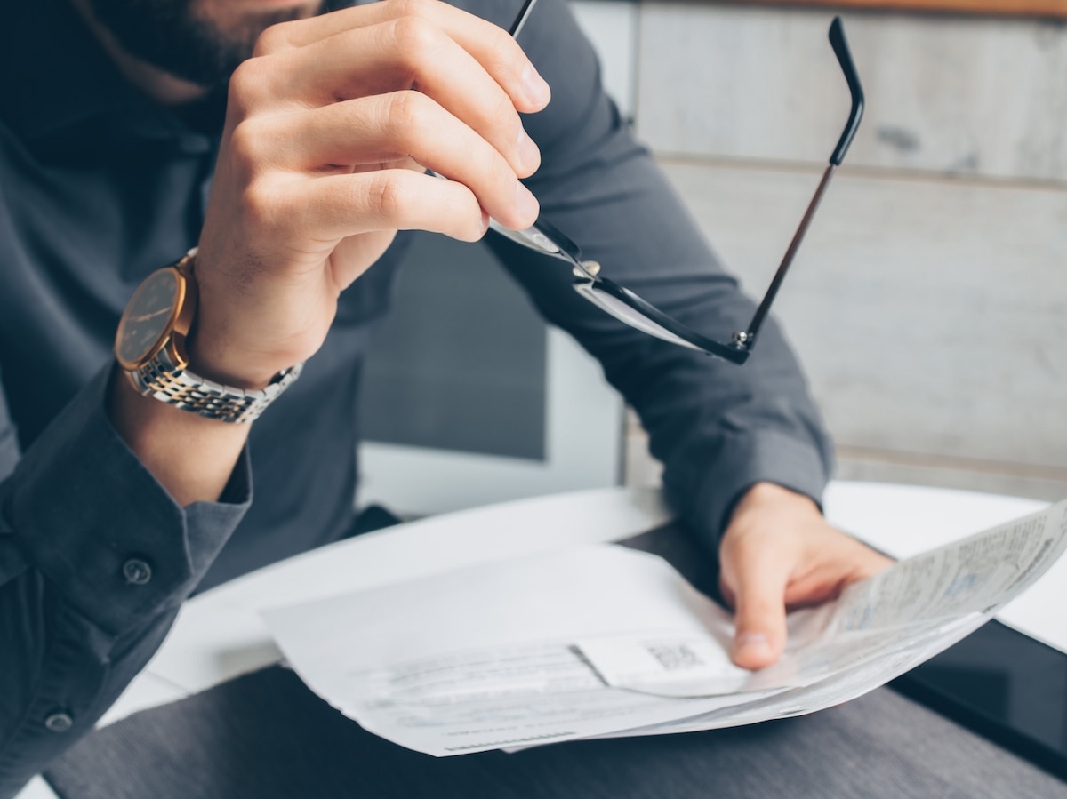 Close-up image of man's arms and hands, holding a piece of paper and eyeglasses.