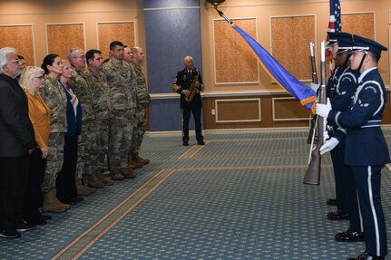 Audience standing on left, Honor Guard presenting colors on right.