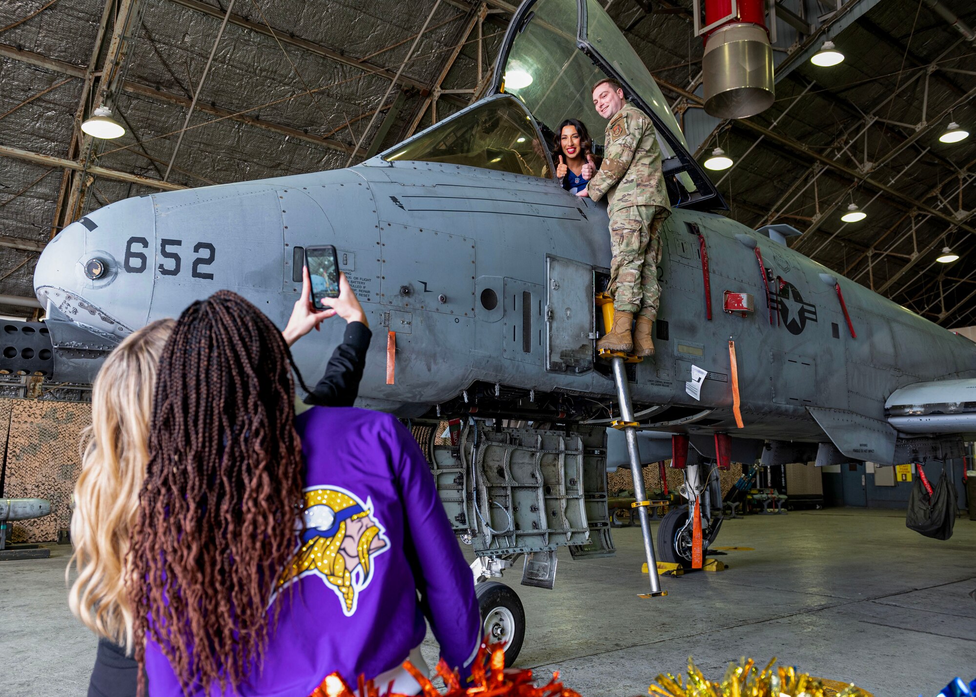 NFL cheerleaders, left, take a photo of U.S. Air Force Tech. Sgt. Ethan Halbert, 51st Maintenance Group loading standardization crew chief, and Kyleigh Creamer, an NFL cheerleader, during the Pro Blitz 2024 unit visit at Osan Air Base, Republic of Korea, Feb. 10, 2024. The NFL Pro Blitz is a week of events for military communities leading up to Super Bowl Sunday. (U.S. Air Force photo by Staff Sgt. Aubree Owens)
